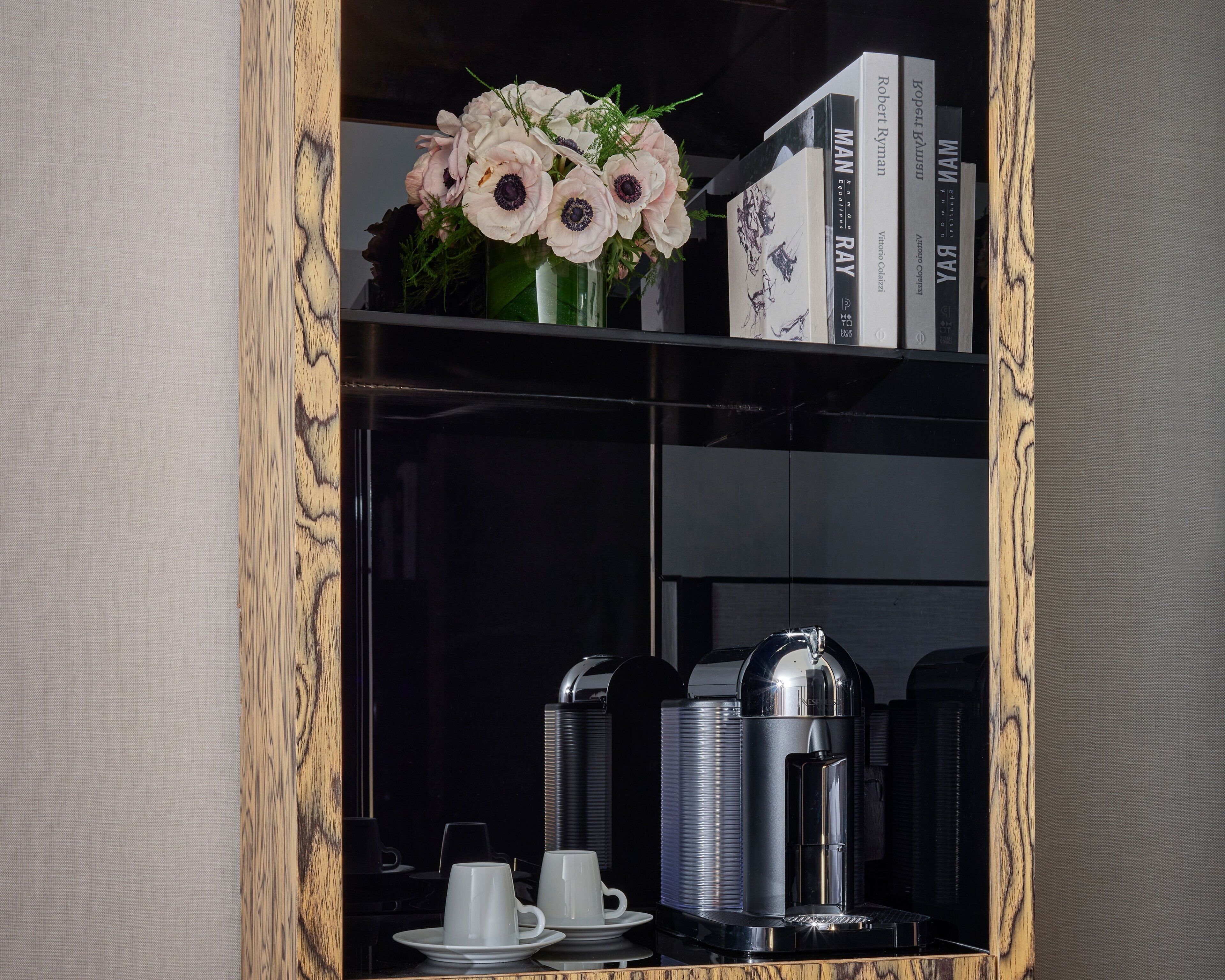 En kaffemaskine, to kopper og en vase med blomster på en hylde.
