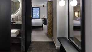 Una camera d'albergo moderna con un grande specchio, una lampada rotonda, un letto, un comodino e una finestra con persiane.
