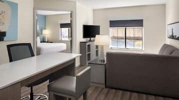 A hotel room with a bed, a desk with a chair, a sofa, a TV, and a window with a view.