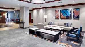 A modern lobby with a sofa set, coffee table, and chairs. There are framed artworks on the wall and a large chandelier. - HYATT house Boston/Waltham (Waltham)