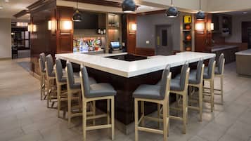 A modern bar area with a large island, bar stools, and a digital screen.
