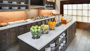 A modern kitchen with a long counter, various food items, and a large window. - HYATT house Boston/Waltham (Waltham)