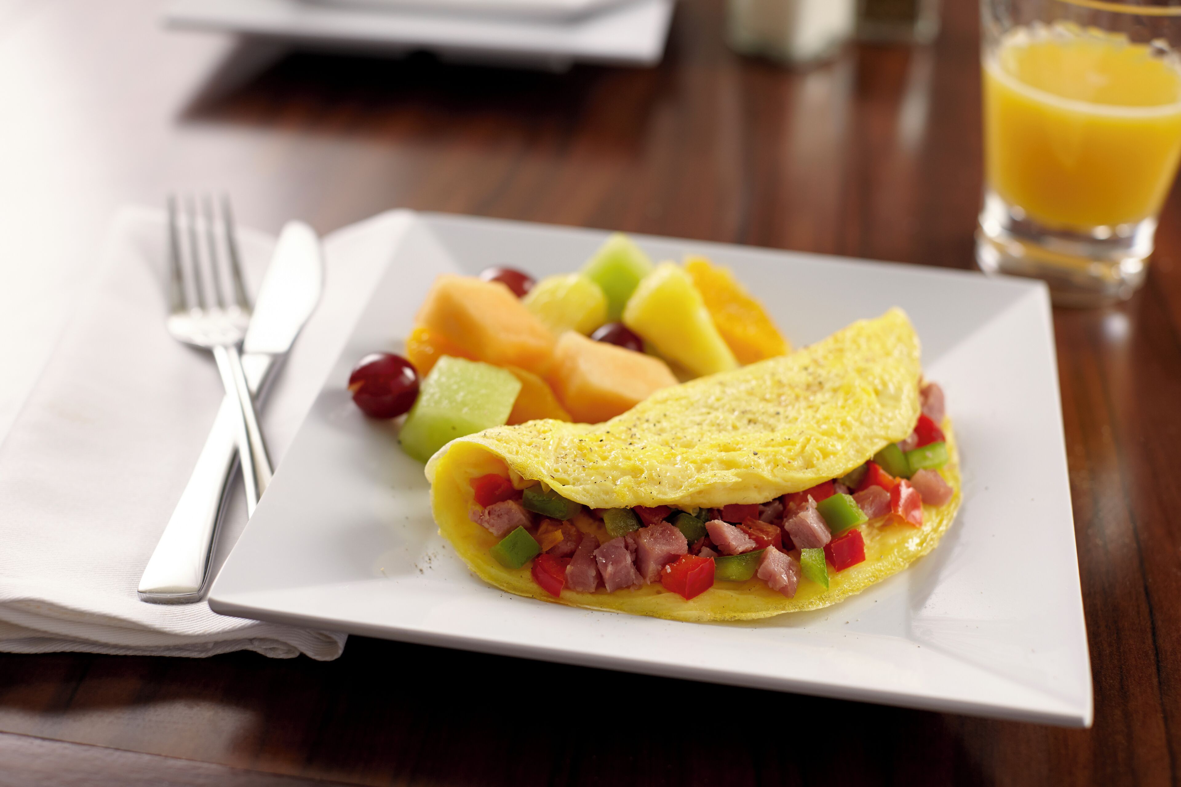 A plate with an omelette, melon, and a glass of orange juice.