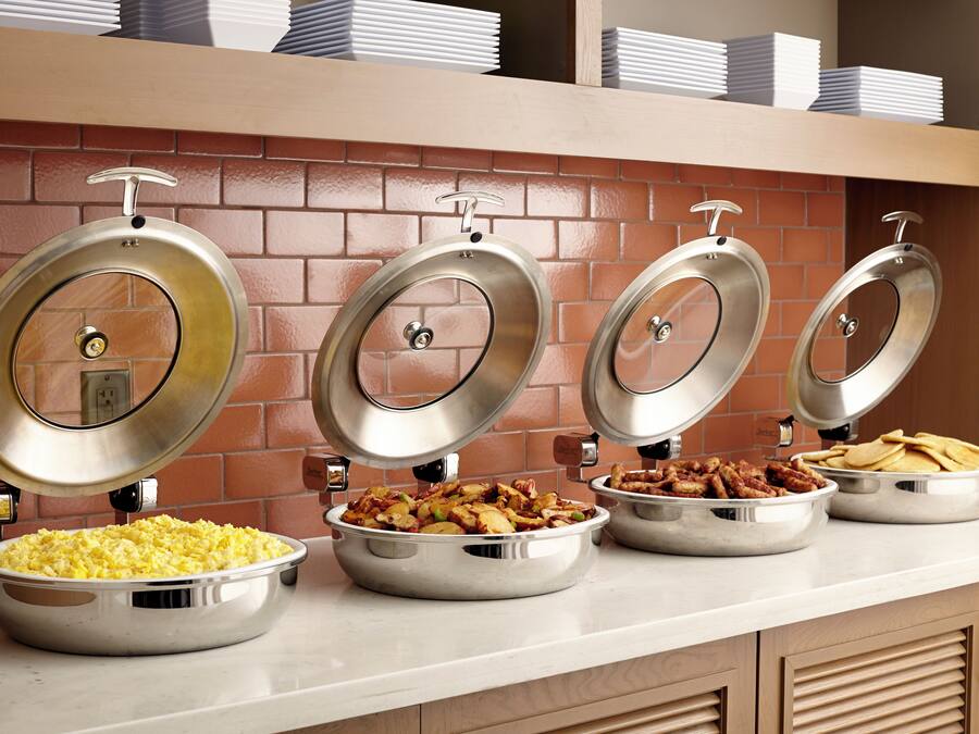 A buffet setup with four stainless steel chafing dishes containing different food items.
