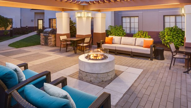 An outdoor patio area with a fire pit, seating, and a grill. - HYATT house Boston/Waltham (Waltham)