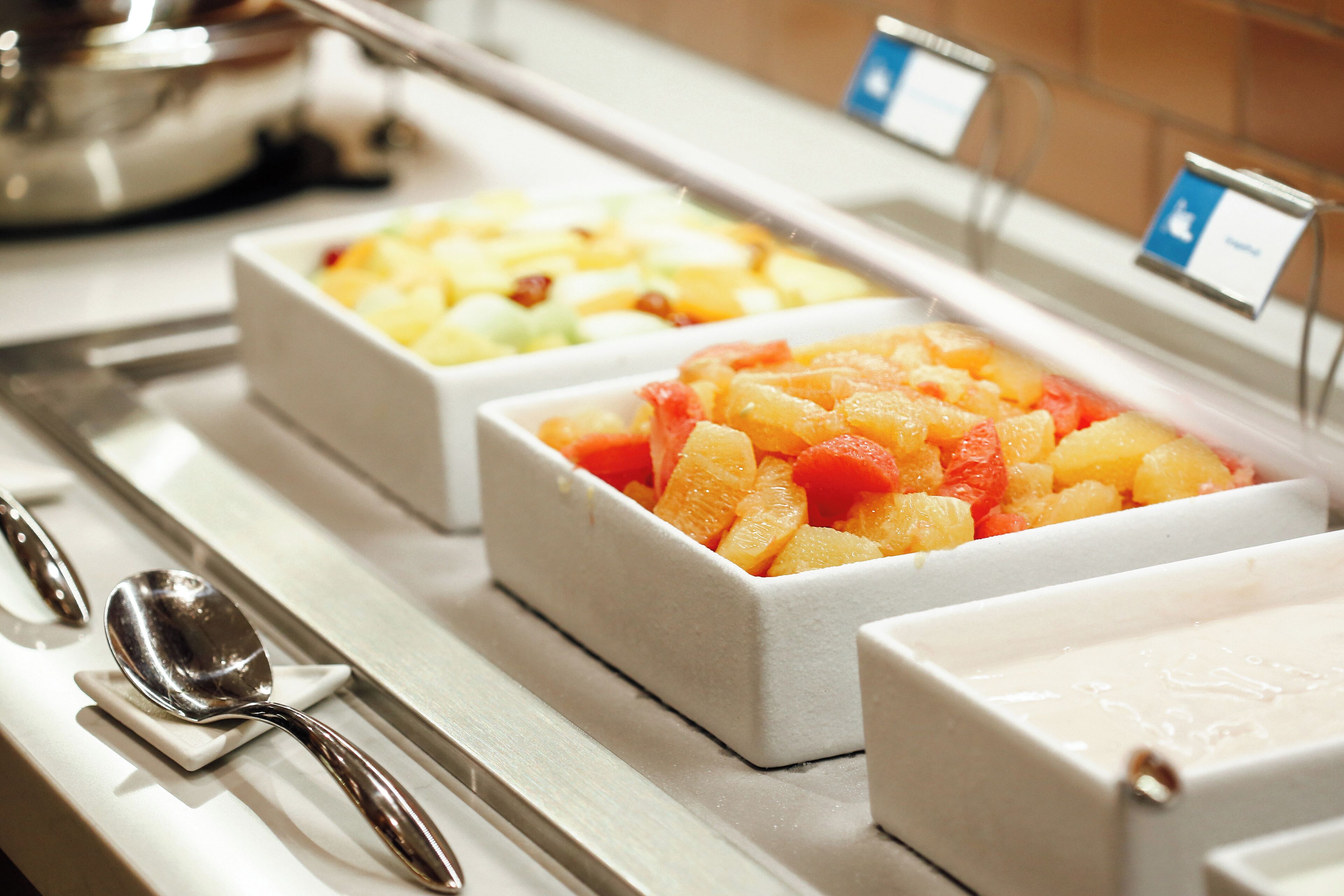 Un buffet proposant différents types de fruits, présentés dans des récipients blancs, avec une cuillère et un petit panneau explicatif.
