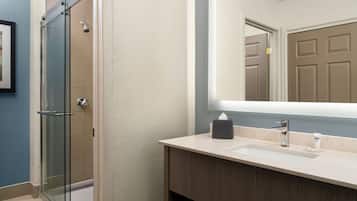 Un baño con cabina de ducha de vidrio, un lavamanos con espejo y una puerta al fondo.