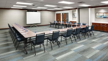 A conference room with a long table, chairs, a projector screen, and a carpeted floor.
