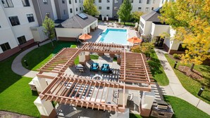 A rooftop pool area with a pergola, seating, and a view of the surrounding buildings. - HYATT house Boston/Waltham (Waltham)