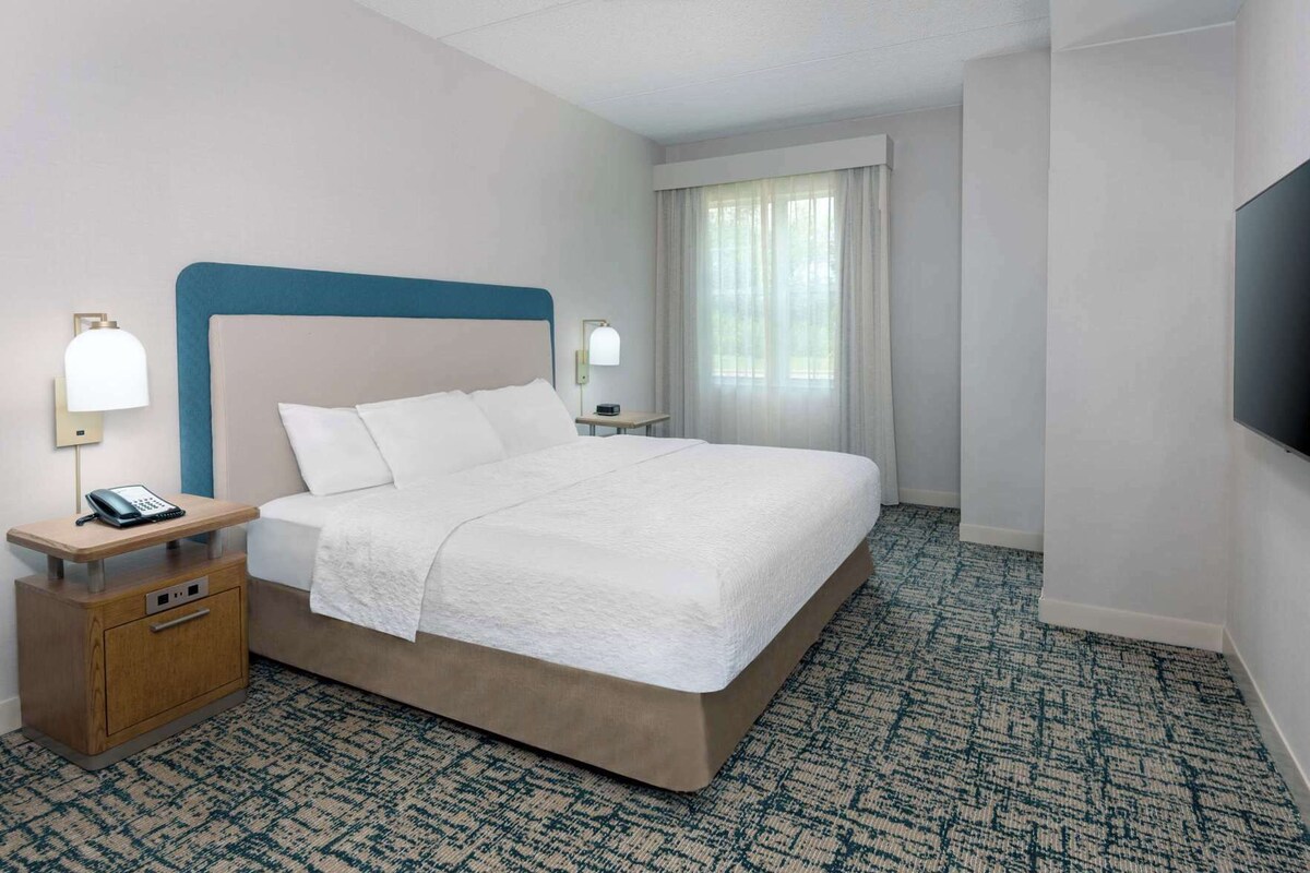A hotel room with a large bed, bedside lamps, a telephone, a small table, and a television on the wall.