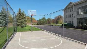Un terrain de basket-ball en plein air, entouré d’un filet, avec un panier de basket et un bâtiment en arrière-plan.