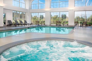 Una amplia piscina interior con sillas de descanso y mesas, rodeada de grandes ventanales.