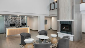 A modern hotel lobby with a reception desk, seating area, and a fireplace. - Homewood Suites by Hilton Buffalo Airport (Buffalo)