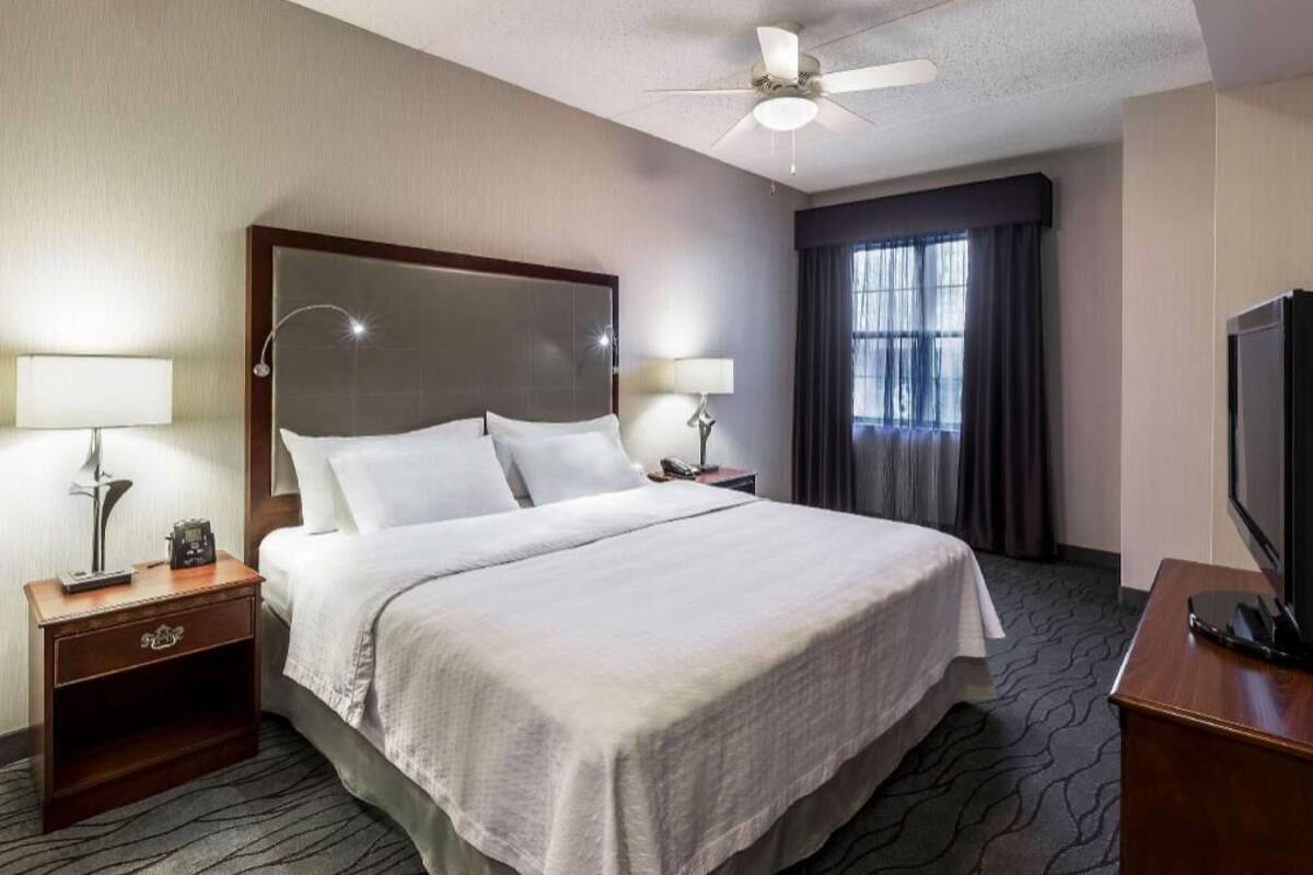 A hotel room with a bed, two bedside tables with lamps, a television, and a ceiling fan.