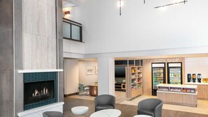 A modern hotel lobby with a fireplace, seating area, and a 'Suite Shop' with refrigerated display cases. - Homewood Suites by Hilton Buffalo Airport (Buffalo)