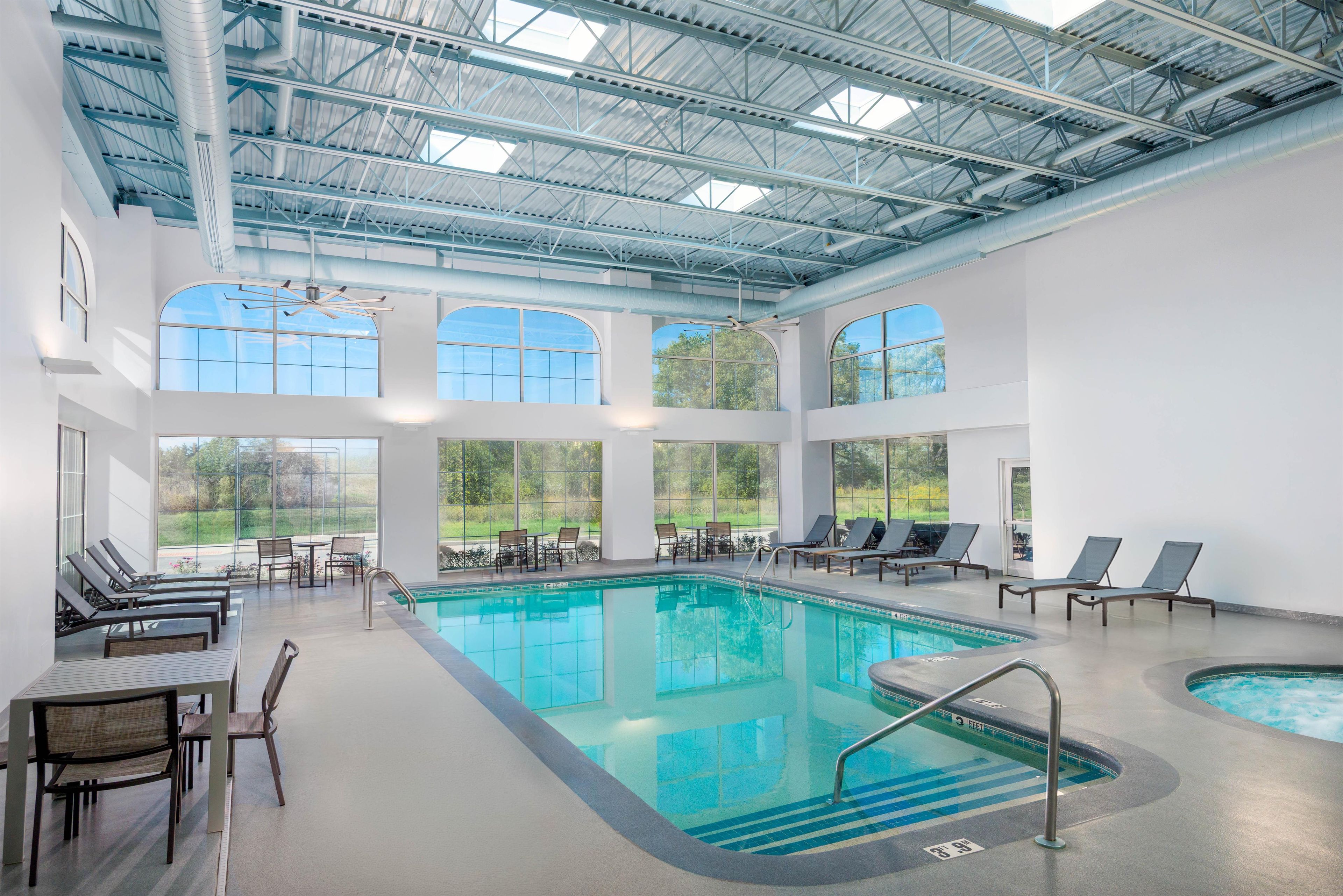 Una amplia piscina interior con varias zonas de descanso y mesas, rodeada de grandes ventanales.