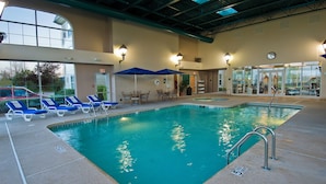 An indoor swimming pool with lounge chairs and umbrellas, surrounded by walls with windows and doors. - Homewood Suites by Hilton Buffalo Airport (Buffalo)