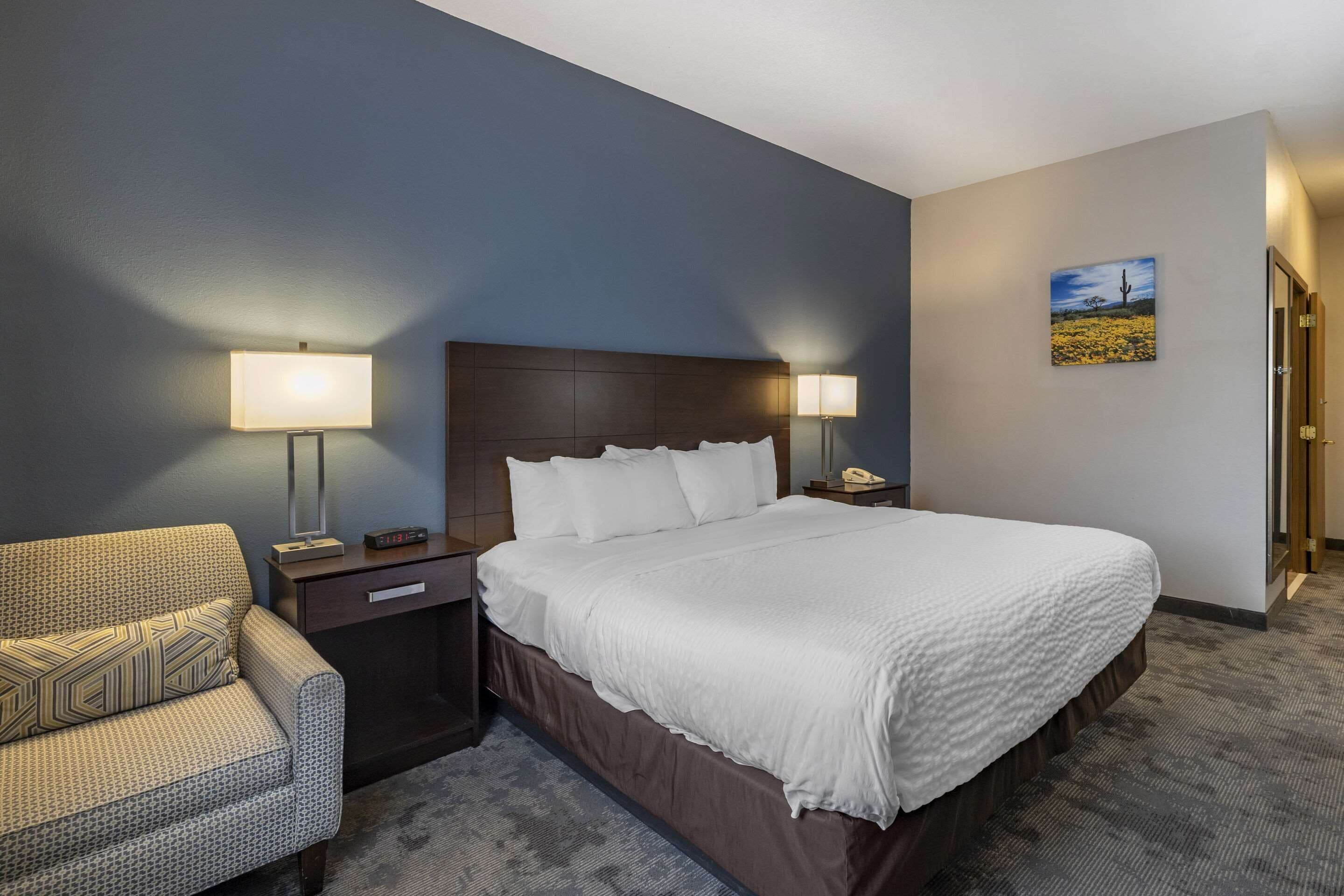A hotel room with a large bed, two bedside tables with lamps, a chair, a nightstand, and a painting on the wall.