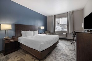A hotel room with a large bed, two bedside tables with lamps, a desk with a flat-screen TV, and a window with curtains.