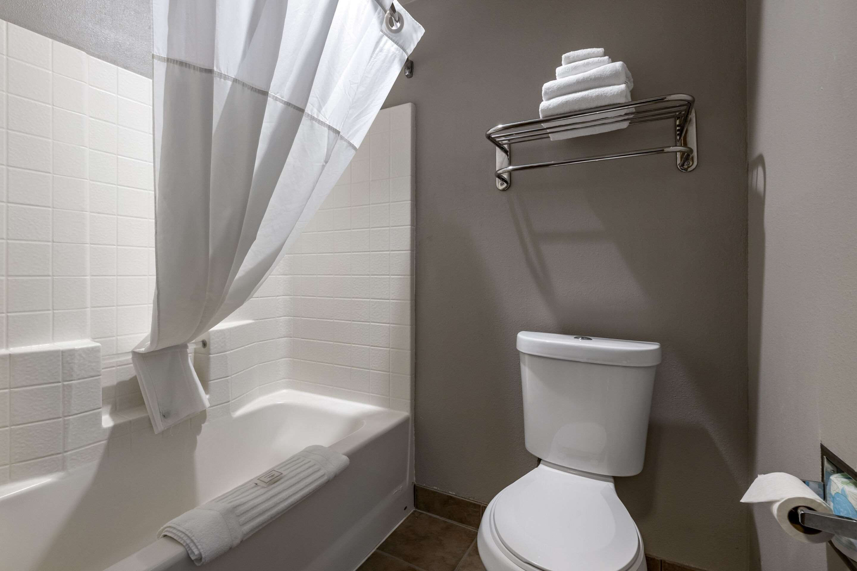 A bathroom with a white bathtub, a toilet, and a towel rack with folded towels.