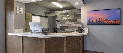 A reception desk with a wooden finish, a mounted computer, and a mounted phone.