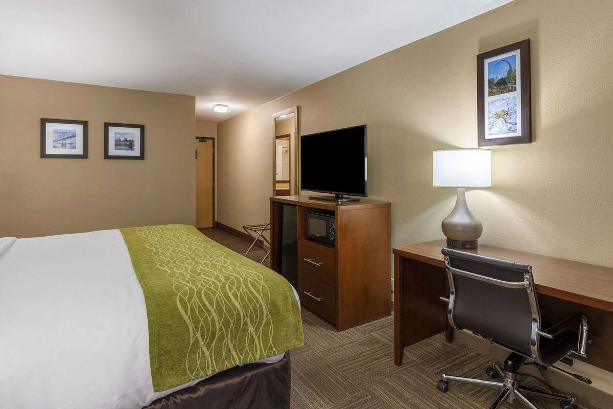 A hotel room with a bed, a desk with a lamp, a television, and a mirror.