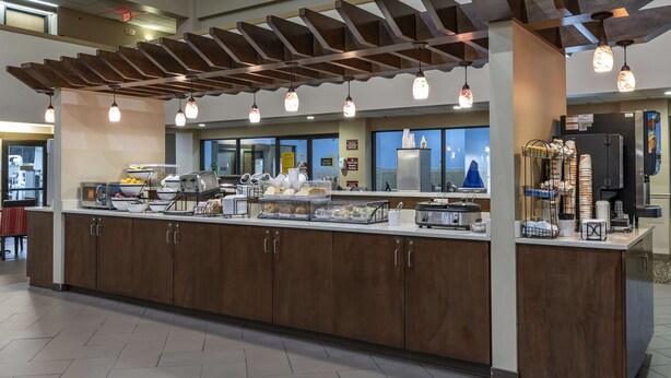 A buffet area with a wooden counter, various food items, and a coffee station. - Comfort Inn Collinsville near St. Louis (Collinsville)