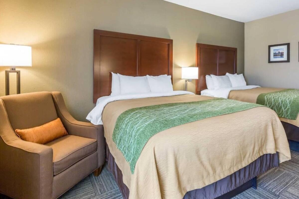 A hotel room with two beds, a chair, lamps, and a framed picture on the wall.