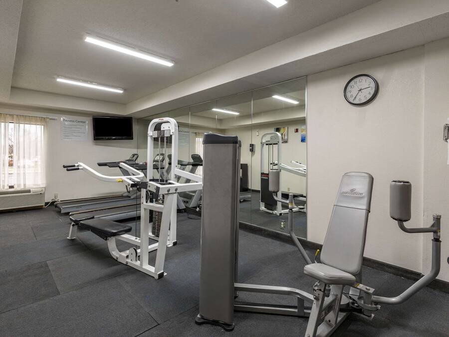 Ein Fitnessraum mit Trainingsgeräten, einem großen Spiegel und einer Wanduhr.