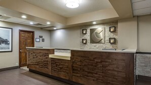 A reception area with a wooden reception desk, a stone wall with a clock, and framed pictures on the wall. - Comfort Inn Collinsville near St. Louis (Collinsville)