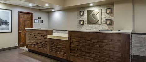 Un área de recepción con un mostrador de madera, una pared de piedra con un reloj y cuadros en la pared.