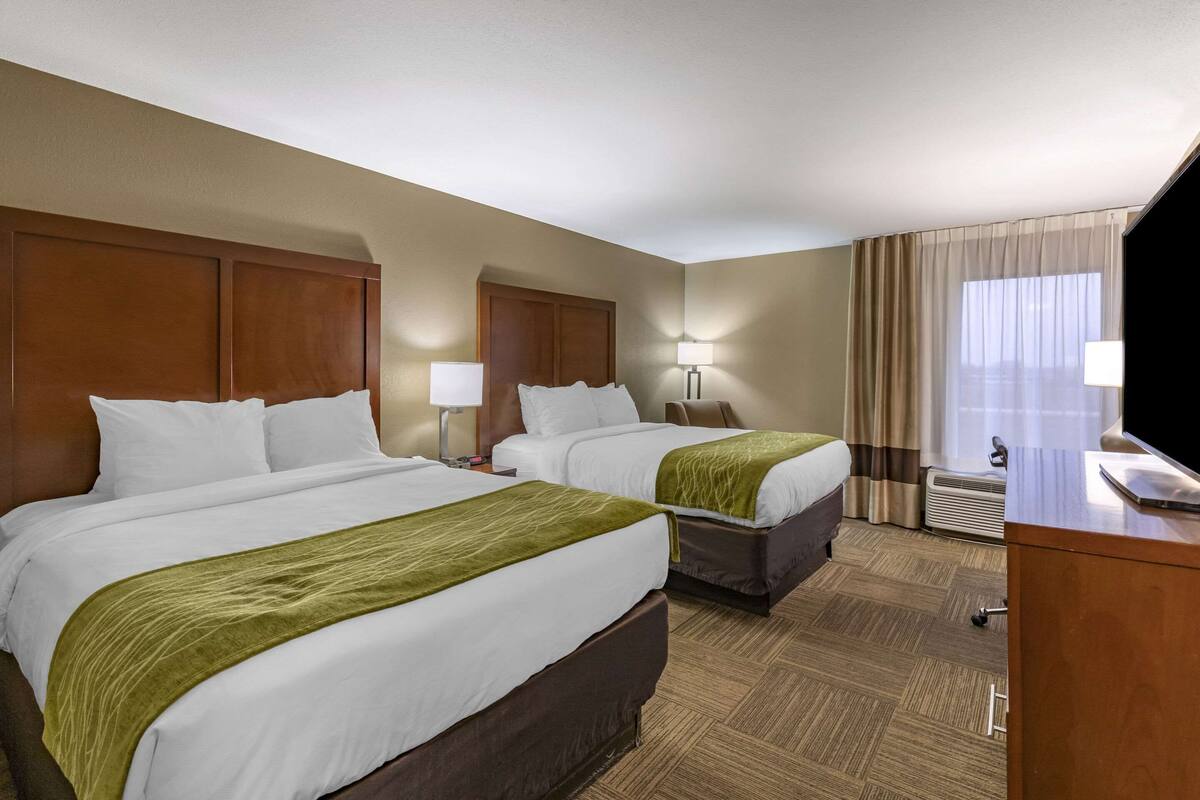 A hotel room with two beds, a desk, a TV, and a window with curtains.