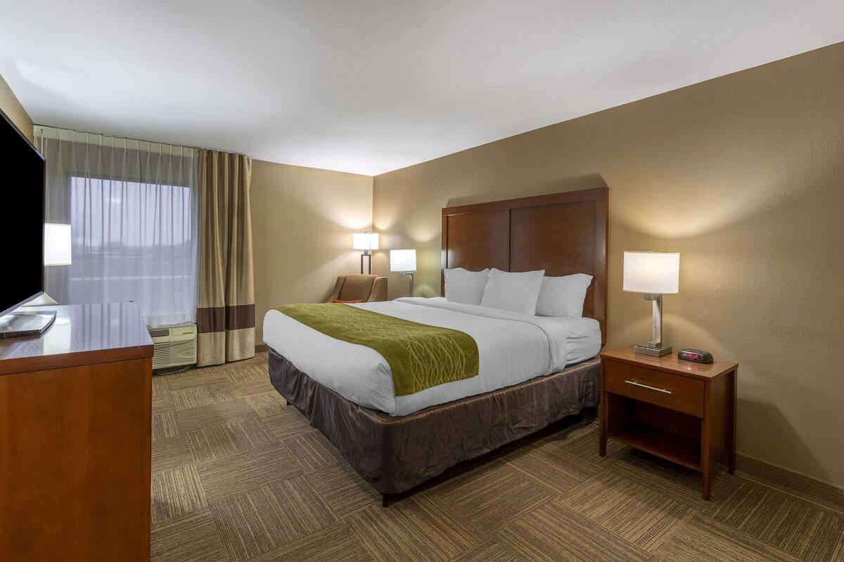 A hotel room with a bed, bedside tables, lamps, a desk, and a TV.