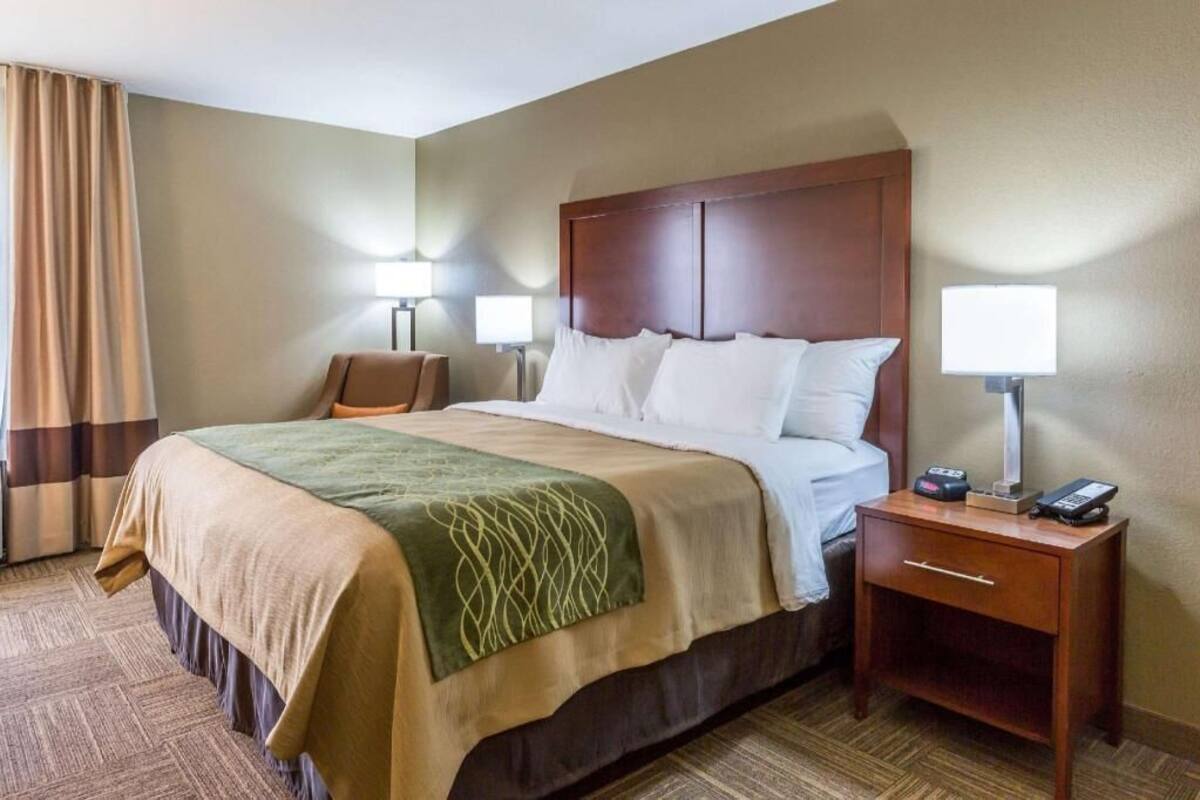 A hotel room with a large bed, two bedside tables, a nightstand, and a lamp.