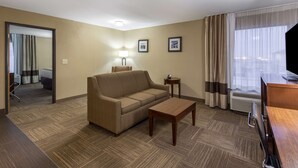 A hotel room with a sofa, a small table, a lamp, and a TV. - Comfort Inn Collinsville near St. Louis (Collinsville)