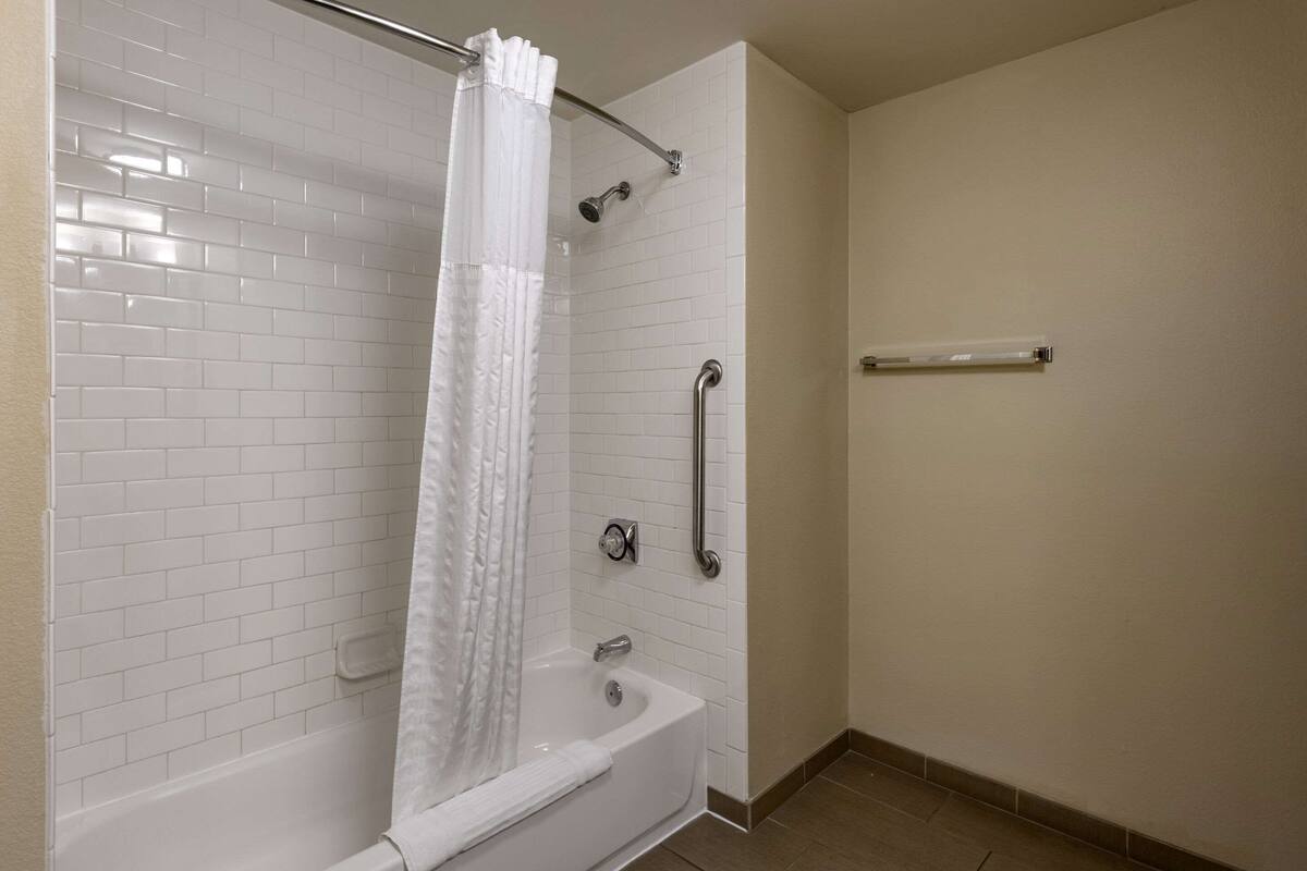 A bathroom with a white bathtub, a shower with a curtain, and a grab bar.