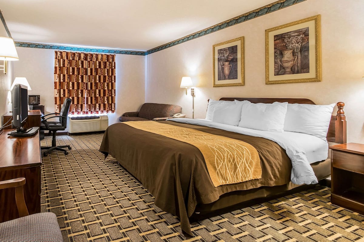 A hotel room with a bed, desk, chair, and a television.
