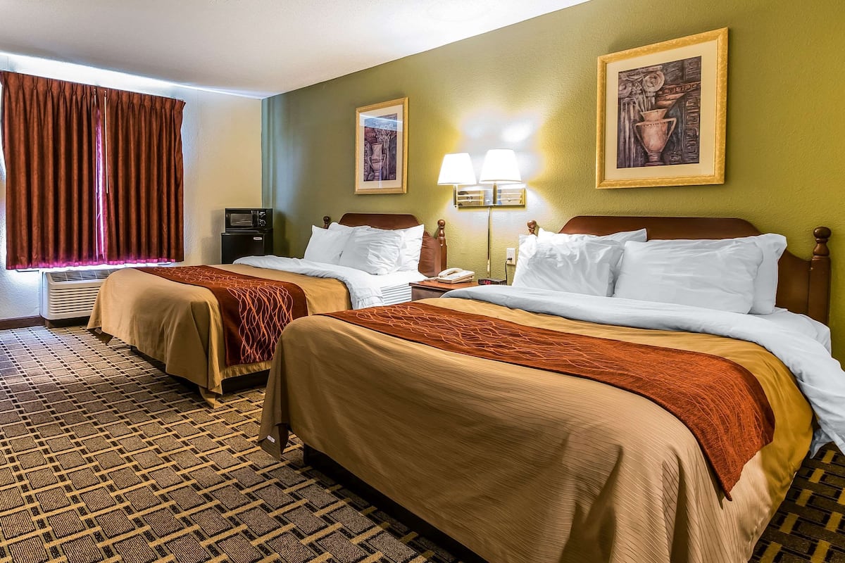 A hotel room with two beds, a desk, a chair, a lamp, and two framed pictures on the wall.