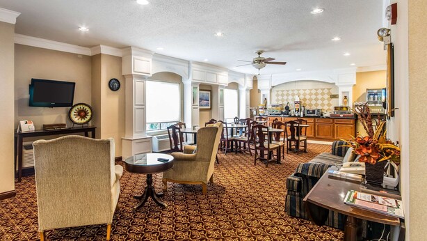 A hotel lobby with a patterned carpet, seating areas, a television, a clock, and a bar area with a coffee machine. - Quality Inn & Suites Evansville North (Evansville)