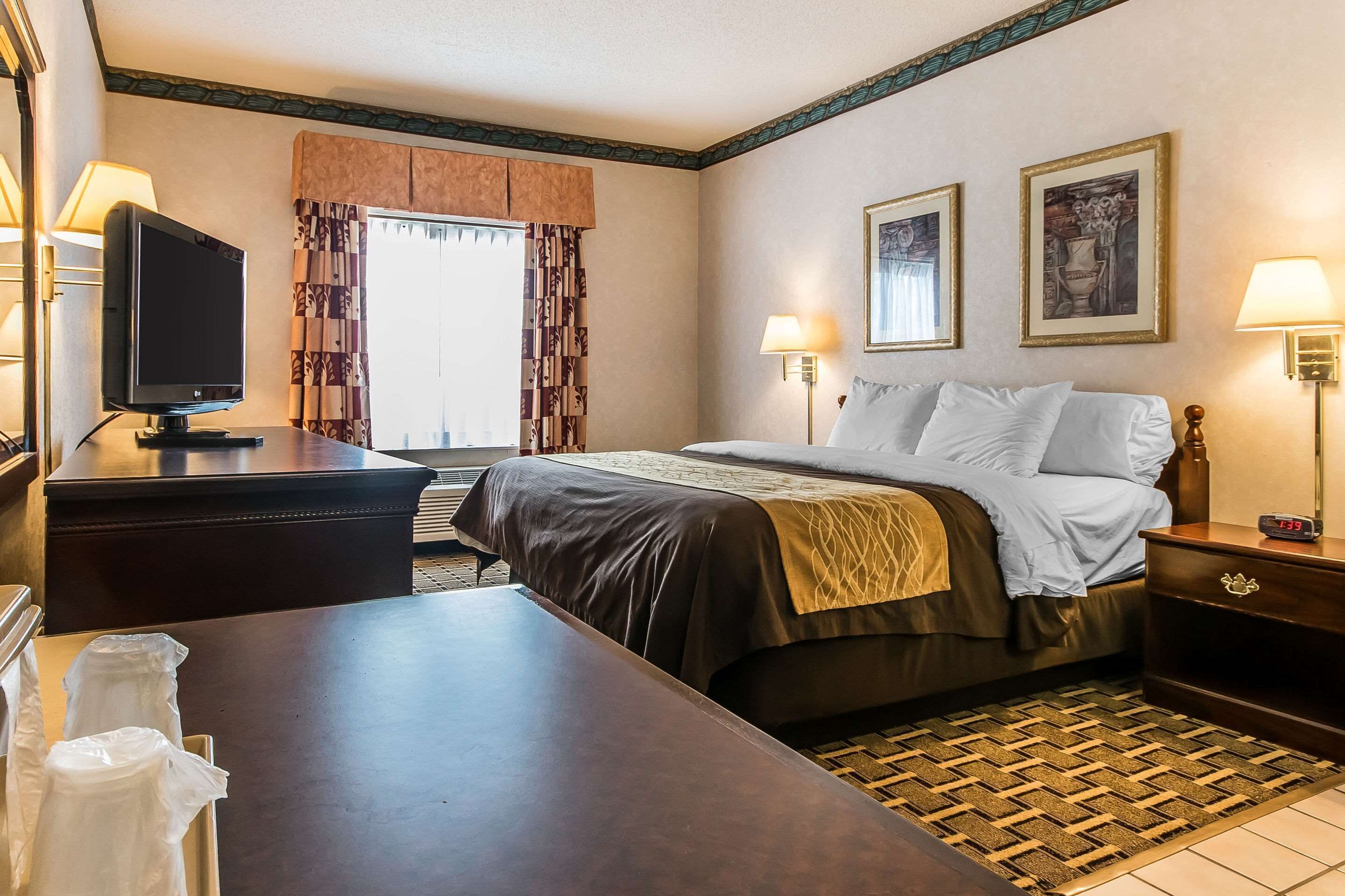 A hotel room with a bed, bedside tables, a television, and a window with curtains.