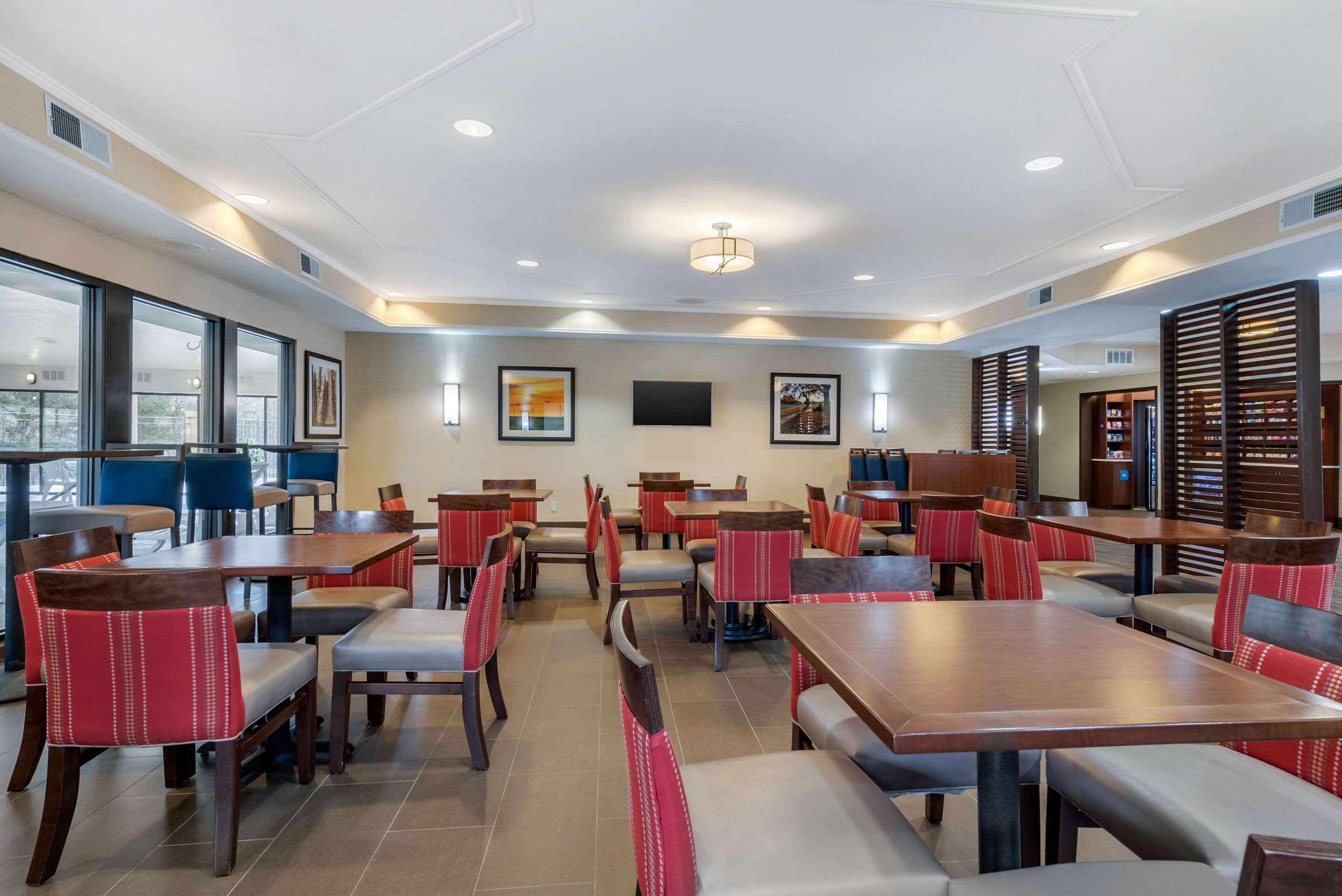 A modern dining area with multiple tables and chairs, large windows, and artwork on the walls.