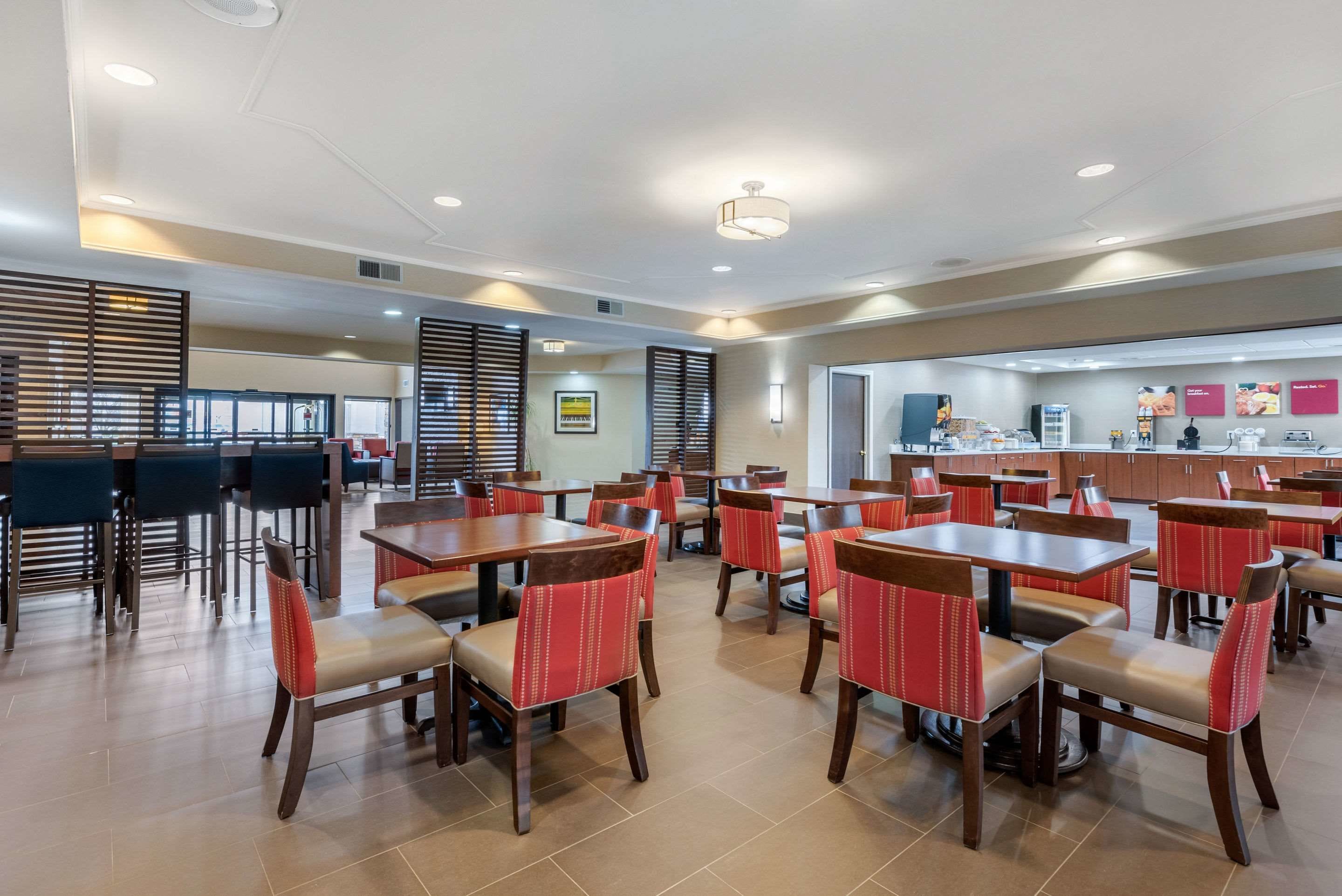 A spacious dining area with multiple tables and chairs, a kitchen area in the background, and a modern ceiling design.