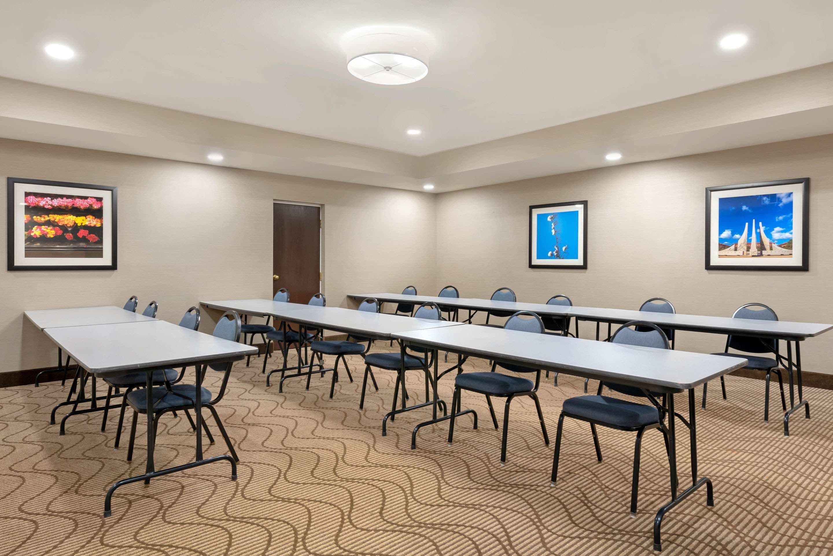 Une salle de conférence avec de longues tables et des chaises, des tableaux encadrés aux murs et un tapis à motifs.