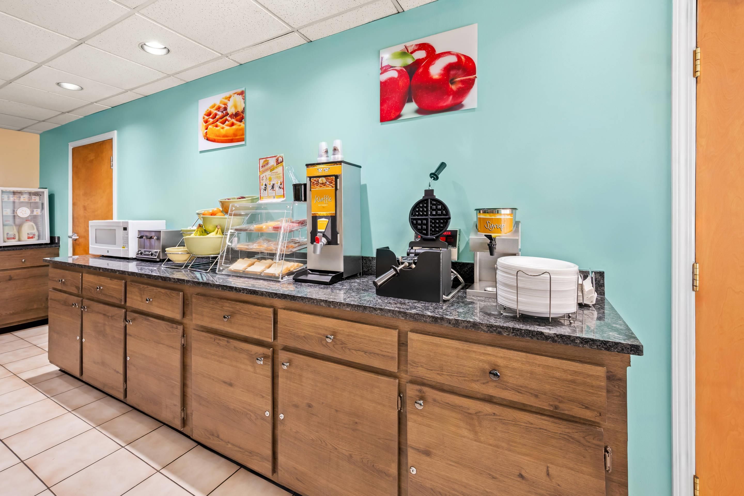 Una barra de desayuno con máquinas para hacer gofres, dispensador de sirope y una máquina de café.