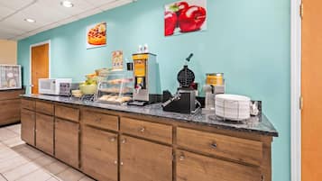 Una barra de desayuno con máquinas para hacer gofres, dispensador de sirope y una máquina de café.