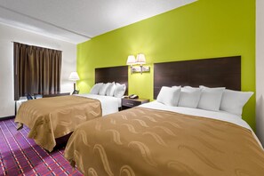 A hotel room with two beds, a nightstand, a lamp, and a window with curtains. - Quality Inn Henderson I-85 (Henderson)