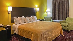 A hotel room with a bed, a nightstand, a chair, and a lamp. - Quality Inn Henderson I-85 (Henderson)