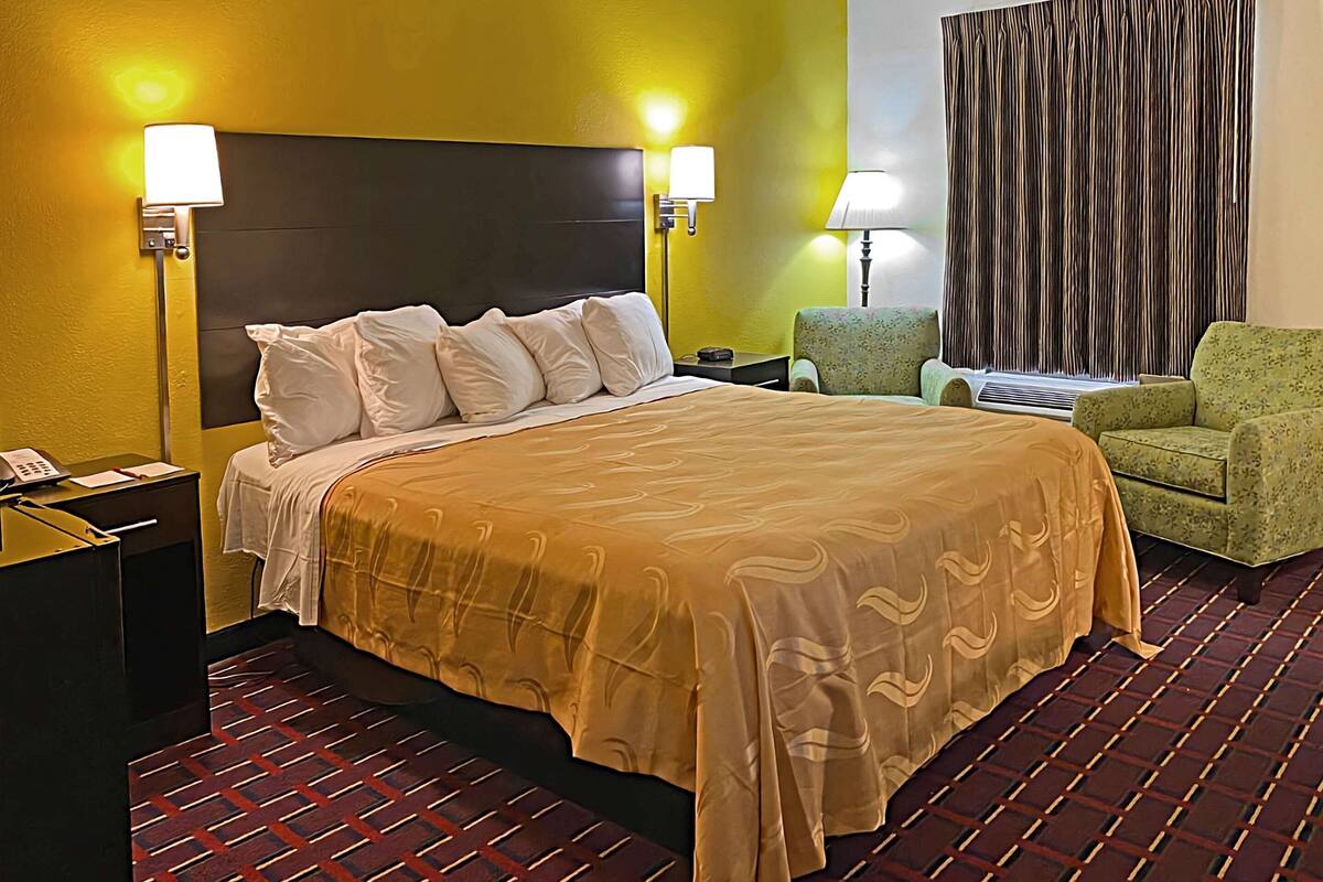 Ein Hotelzimmer mit Bett, Nachttisch, Stuhl und Lampe.