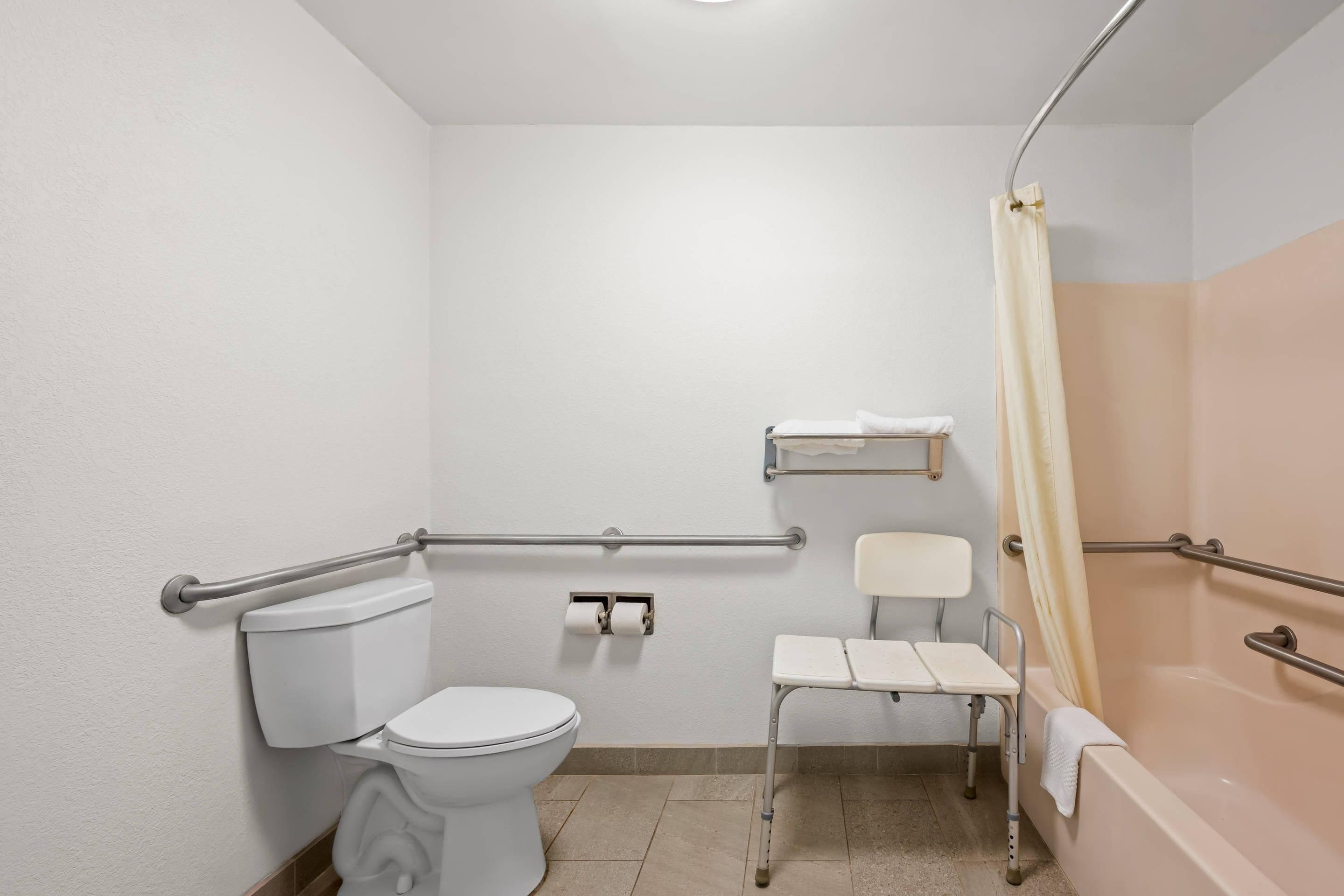 A standard bathroom with a toilet, a handrail, a shower area, and a grab bar.