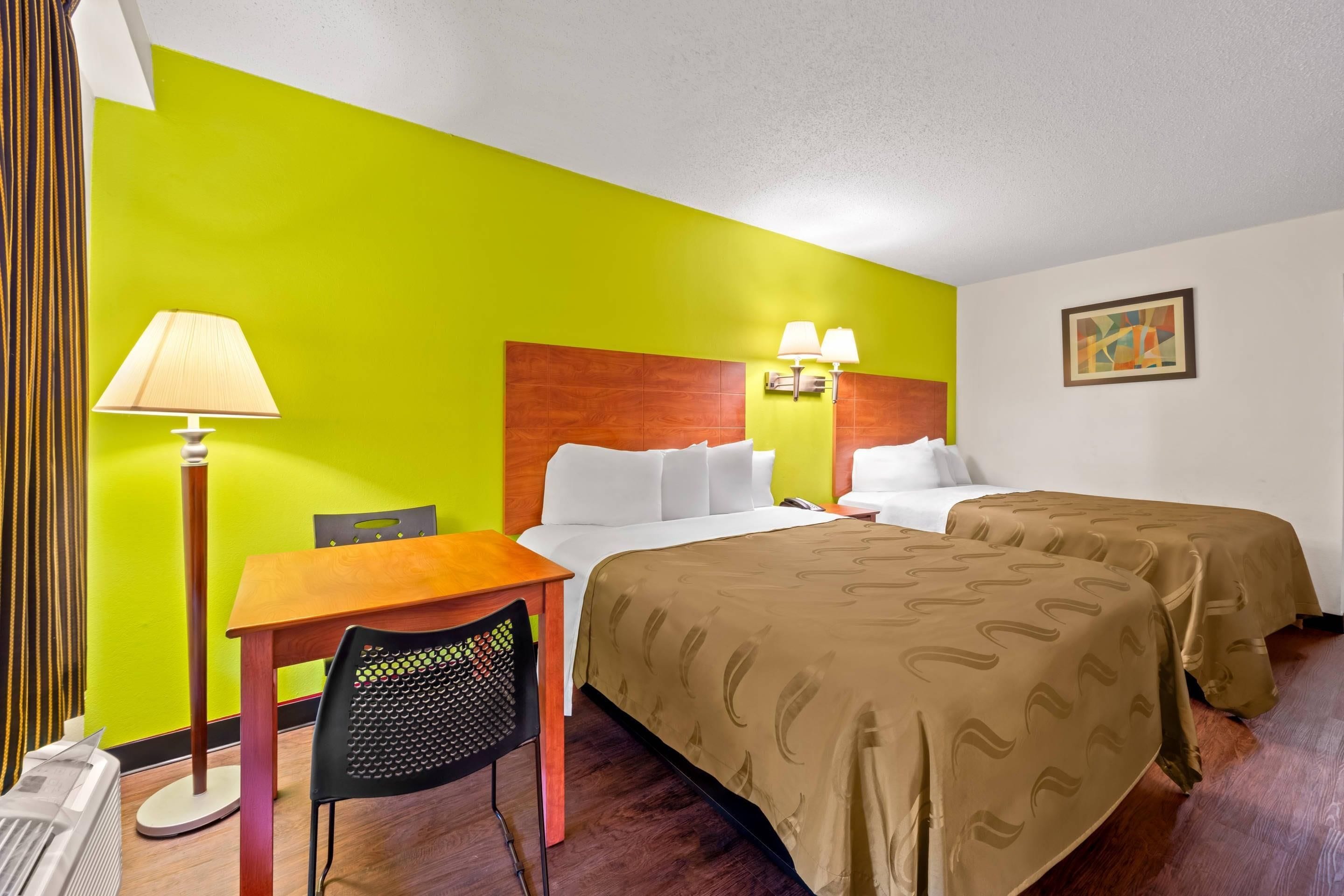 A hotel room with a bed, bedside tables, a desk, a chair, and a lamp.